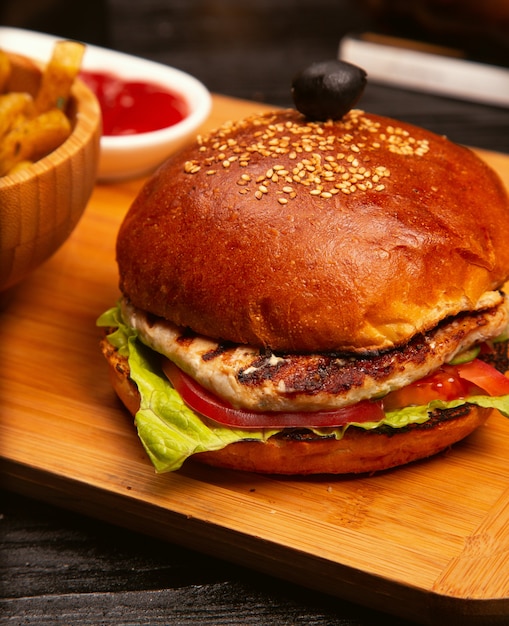 Hühnerfleischburger mit tomatenscheiben und kopfsalat diente mit pommes-frites, ketschup und majonäse auf hölzernem brett Kostenlose Fotos
