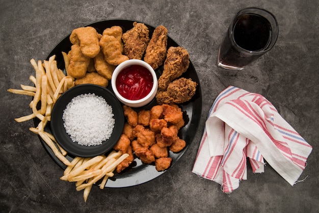 Hühnernuggets; gebratenes hähnchenkeule; knuspriges hühnerpopcorn; pommes-frites mit softdrink und serviette auf konkretem hintergrund Kostenlose Fotos
