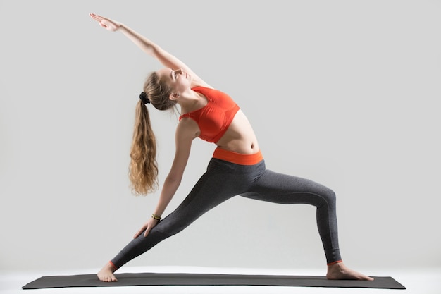 Junge attraktive frau steht in reverse warrior pose, grau st Kostenlose Fotos