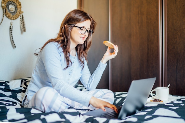 Junge frau, die vom bett zu hause mit computer arbeitet