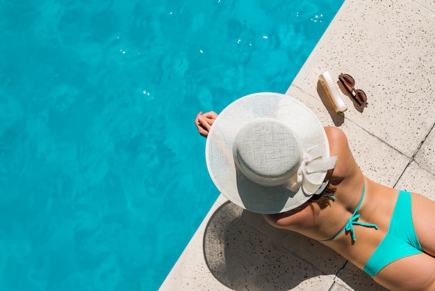 Junge frau im bikini, der auf poolside ein sonnenbad nimmt Kostenlose Fotos