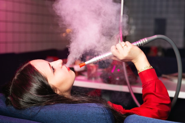 Junge frau raucht eine wasserpfeife oder shisha im club oder in der bar rauchen Premium Fotos