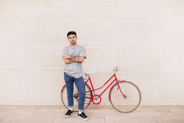 Junge mit den gefalteten armen, die nahes rotes fahrrad