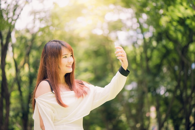 Junge Schone Asiatische Frauen Mit Langen Braunen Haaren Ein Selfie Auf Ihrem Handy Im Park Naturliche Beleuchtung Lebendige Farben Kostenlose Foto