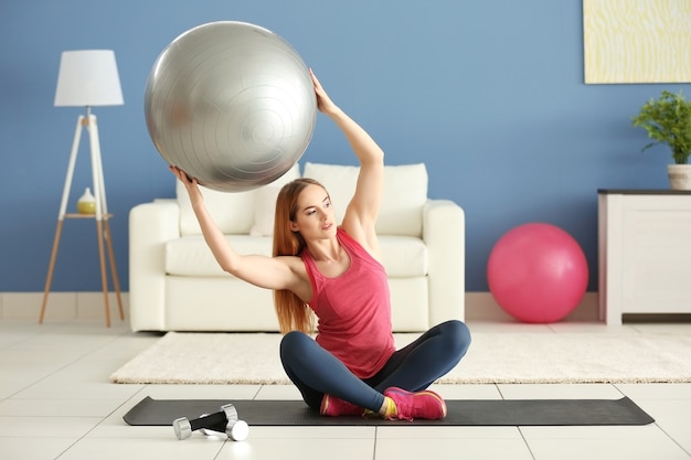 Junge sportlerin, die übungen mit ball auf einer matte zu