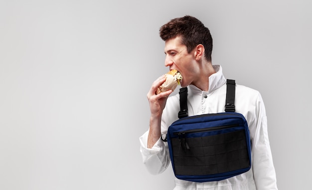 Junge stilvolle männliche arbeitskraft mit kastenplattformbeutel isst einen geschmackvollen saftigen burger auf einem weißen hintergrund Premium Fotos