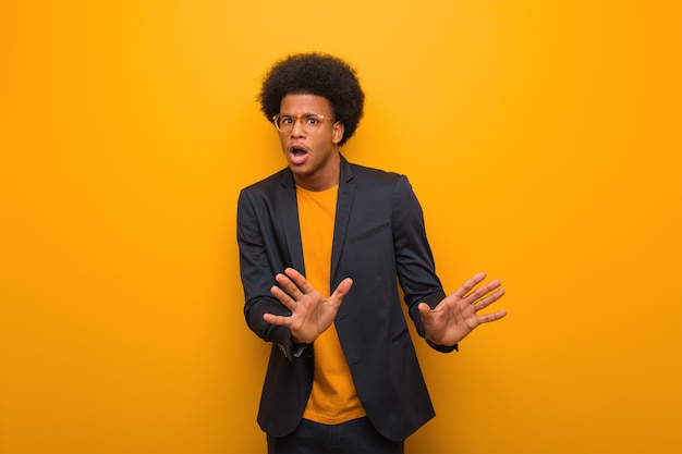 Junger geschäftsafroamerikanermann über einer orange wand etwas zurückweisend, eine geste des ekels tuend Premium Fotos