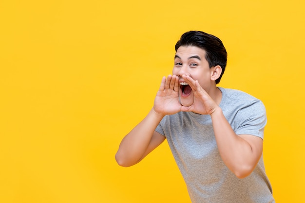 Junger glucklicher asiatischer mann, der mit handschale um mund schreit ... image