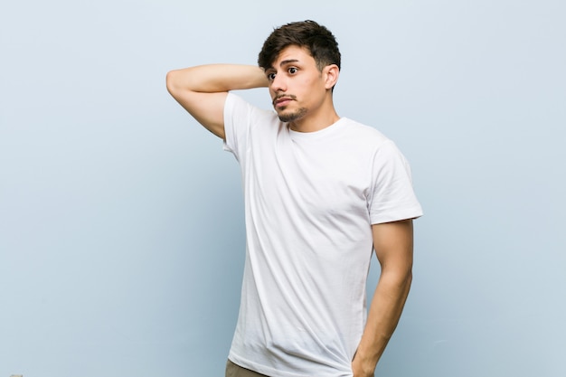 Junger mann, der ein weißes t-shirt berührt zurück vom kopf trägt, eine wahl denkt und trifft Premium Fotos