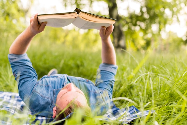 Junger mann, der interessantes buch bei der entspannung im gras liest