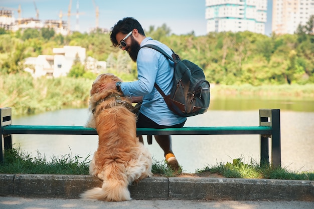 Junger mann, der mit seinem hund auf dem stuhl im park sitzt