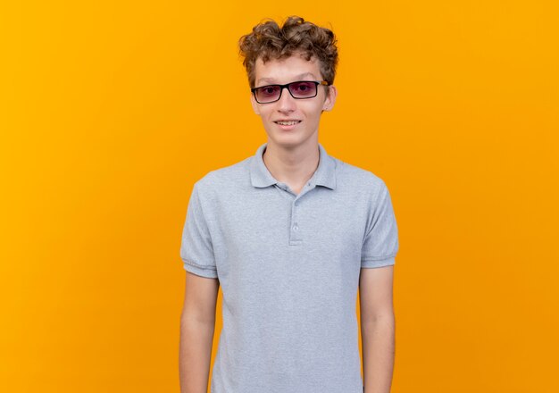 Junger Mann In Der Schwarzen Brille Die Graues Poloshirt Mit Lacheln Auf Gesicht Uber Orange Tragt Kostenlose Foto