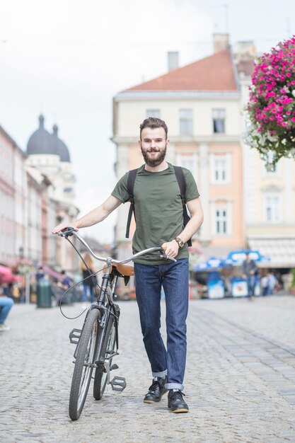 Junger mann mit dem fahrrad gehend auf straße Kostenlose