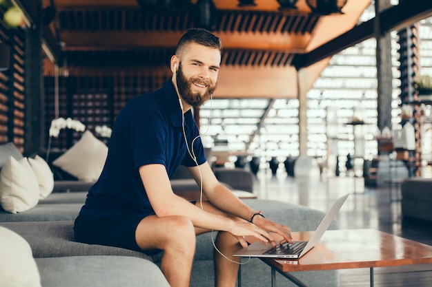 Junger mann mit einem bart arbeitet in einem café, freelancer nutzt einen laptop, macht ein projekt Kostenlose Fotos