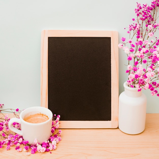 Kaffeetasse und rosa vase des schätzchens des atems nahe dem leeren hölzernen schiefer auf schreibtisch gegen wand Kostenlose Fotos