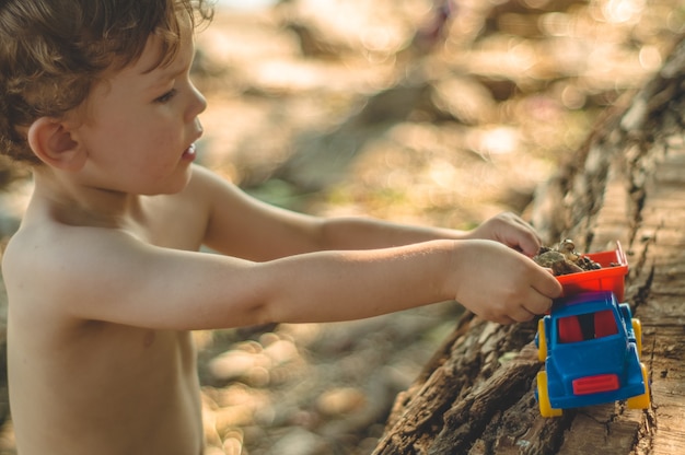 Kind Spielt Im Freien Kind Wir Giessen Den Sand In Den Roten Lastwagen Kinder Strassenspiele Ein Junge Spielt Mit Einer Maschine Auf Dem Grossen Baumstamm Premium Foto