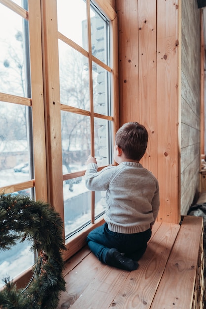 Kleiner junge, der aus dem fenster heraus schaut, das