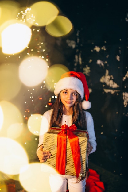 Kleines mädchen, das durch weihnachtsbaum sitzt und geschenke auspackt Kostenlose Fotos