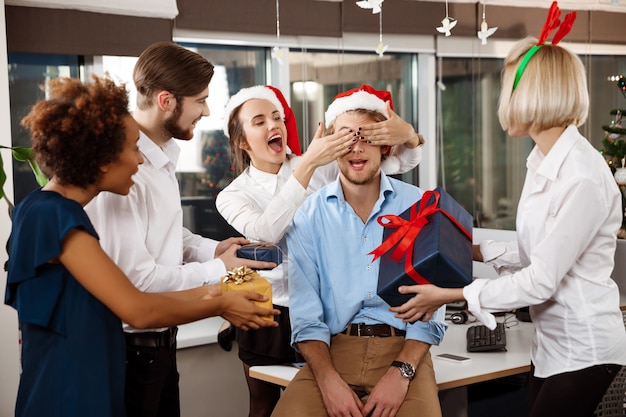 Kollegen feiern weihnachtsfeier im büro lächelnd geschenke geben