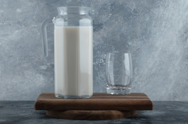 Krug mit frischer milch und glas wasser auf holzbrett