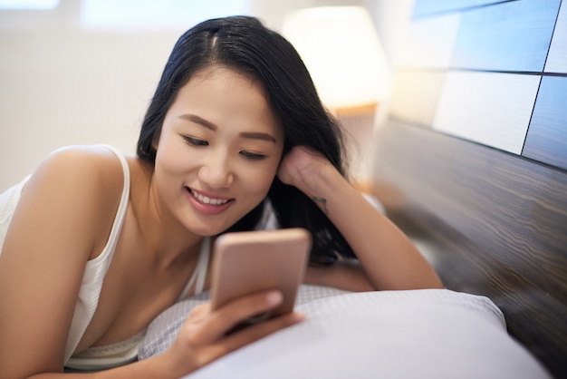 Kühlende frau im bett unter verwendung des telefons Kostenlose Fotos