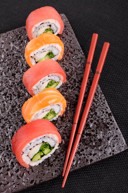 Lachs thunfisch-sushi-rolle mit stäbchen auf einem schwarzen teller ...