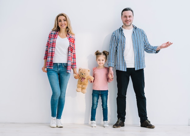 Lächelnde eltern mit ihrer tochter, die gegen weiße wand steht Kostenlose Fotos