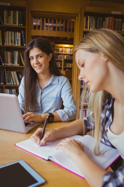 Lächelnde studenten, die laptop in der bibliothek verwenden Premium Fotos