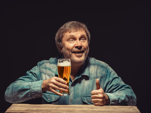 Lächelnder mann im jeanshemd mit glas bier Kostenlose Foto