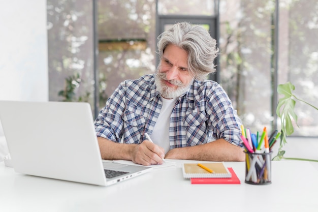 Lehrer Der Am Schreibtisch Bleibt Der Auf Notizbuch Schreibt Und Laptop Betrachtet Kostenlose Foto