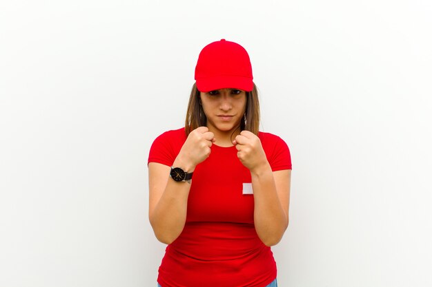 Lieferungsfrau, die überzeugt, verärgert, stark und aggressiv, mit den fäusten bereit schaut, in verpackenstellungsweiß zu kämpfen Premium Fotos