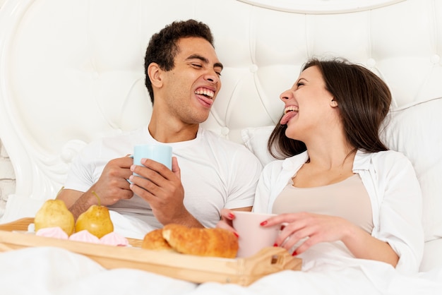 Lustige paare des mittleren schusses, die im bett frühstücken