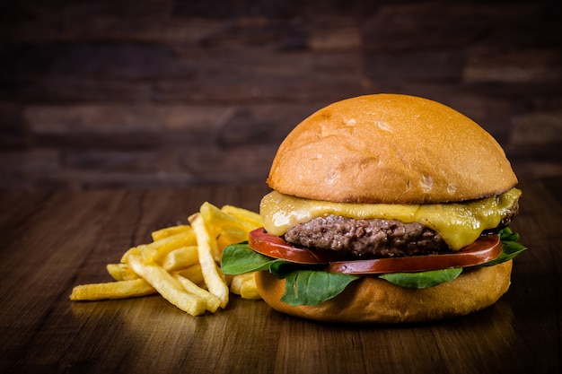 Machen sie rindfleischburger mit käse, raketenblättern und pommes-frites auf hölzerner tabelle in handarbeit Premium Fotos