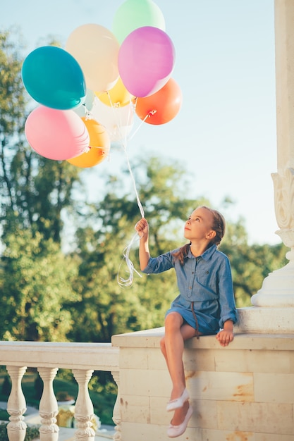 Mädchen, das bunte luftballons hält, die zu ihnen schauen Kostenlose Foto
