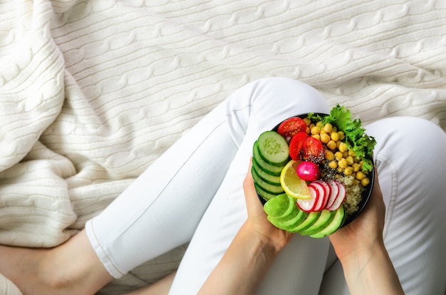 Mädchen in den weißen jeans hält in der handgabel, vegane frühstücksmahlzeit in der schüssel mit avocado, quinoa, gurke, rettich, salat, zitrone, kirschtomaten, kichererbse Premium Fotos