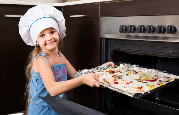 Mädchen in kochmütze in der nähe von ofen mit pizza PremiumFoto