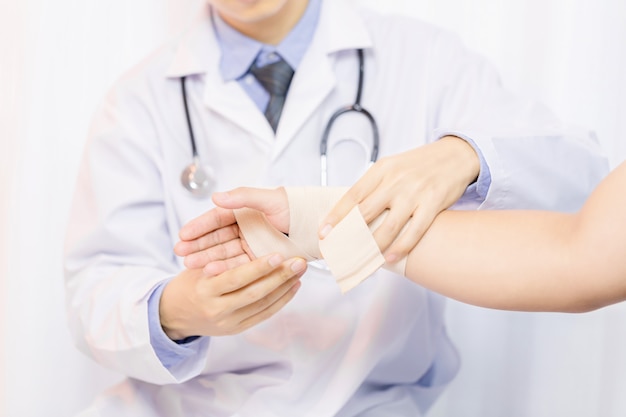 Männlicher doktor, der gaze auf die hand des jungen mannes in klinik, nahaufnahme einsetzt. erste hilfe Kostenlose Fotos
