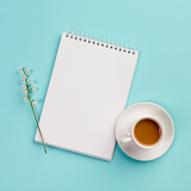 Maiglöckchenblumenzweig auf weißem gewundenem notizblock mit kaffeetasse auf blauem hintergrund Kostenlose Fotos