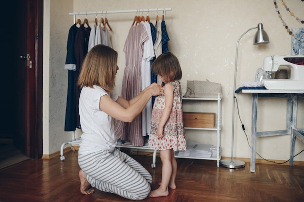 Mama kleidet ihre tochter in ein kleid. morgen. | Premium-Foto