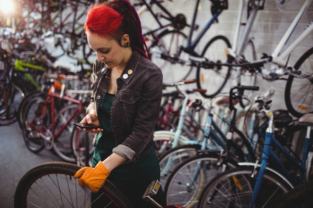 Mechaniker mit Handy während Fahrrad reparieren Download