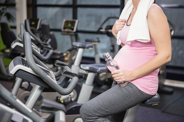 Mittlerer abschnitt der schwangeren frau auf hometrainer an der turnhalle Premium Fotos