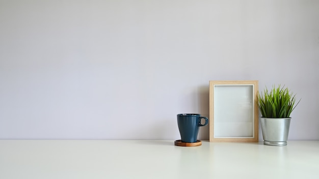 Modell-kopienraumschreibtischfotorahmen und -kaffee mit blumentopf auf weißem schreibtisch. Premium Fotos