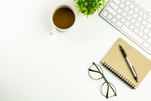 Moderner weißer schreibtisch mit einer computertastatur, einem stift, einem notizbuch und einem tasse kaffee. Premium Fotos