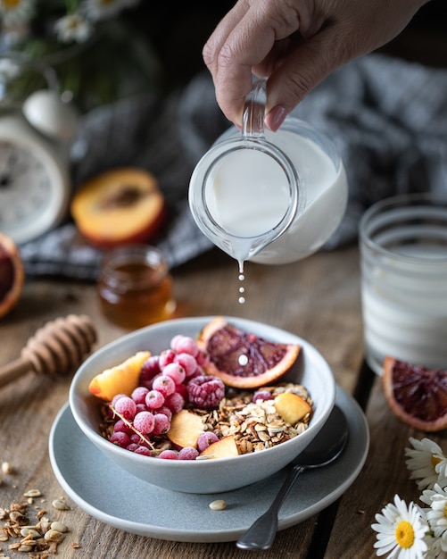 Müsli frühstück mit beeren und früchten und honig und ein glas milch ...