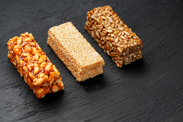 Müsliriegel mit erdnüssen, indischem sesam und sonnenblumensamen auf einem schneidebrett auf einer dunklen steintabelle. von oben betrachten. drei verschiedene bars Premium Fotos