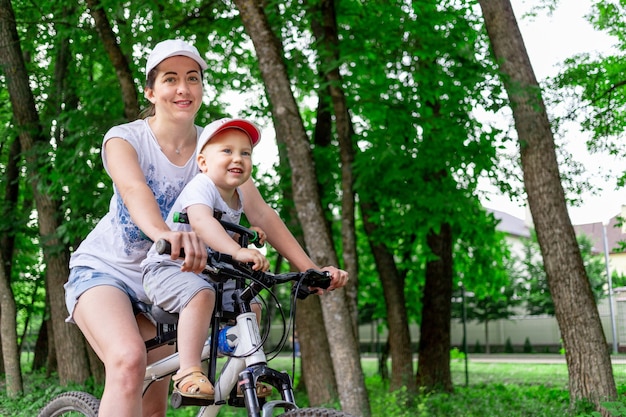 Mutter und sohn fahren fahrrad, mutter trägt im sommer ein