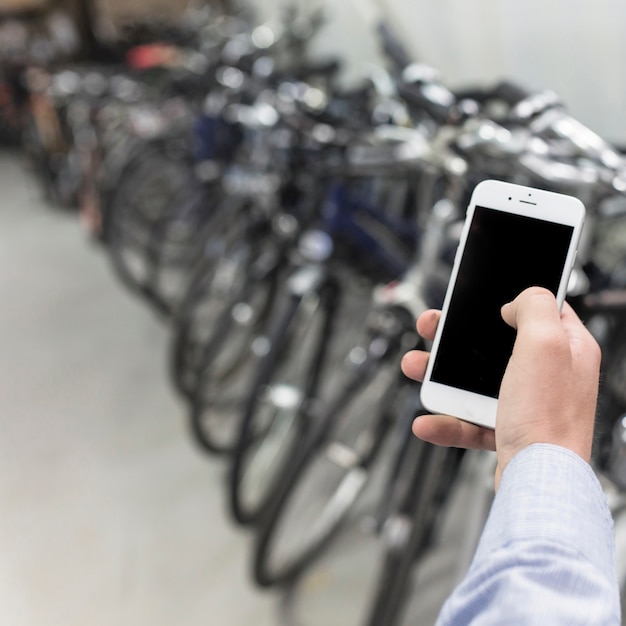 Nahaufnahme der hand eines mannes unter verwendung des mobiltelefons in der fahrradwerkstatt Kostenlose Fotos
