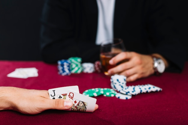 Nahaufnahme der hand eines spielers mit spielkarte auf roter pokertabelle Kostenlose Fotos