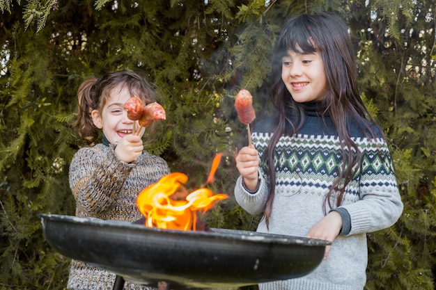 Nahaufnahme des grills vor zwei glücklichen mädchen, die würste halten Kostenlose Fotos