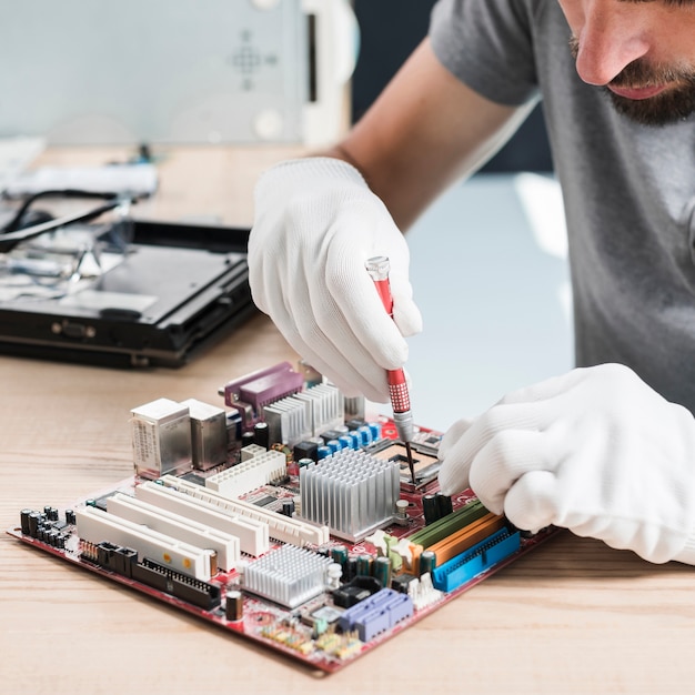 Nahaufnahme einer männlichen technikerhand, die computermotherboard auf hölzernem schreibtisch repariert Kostenlose Fotos